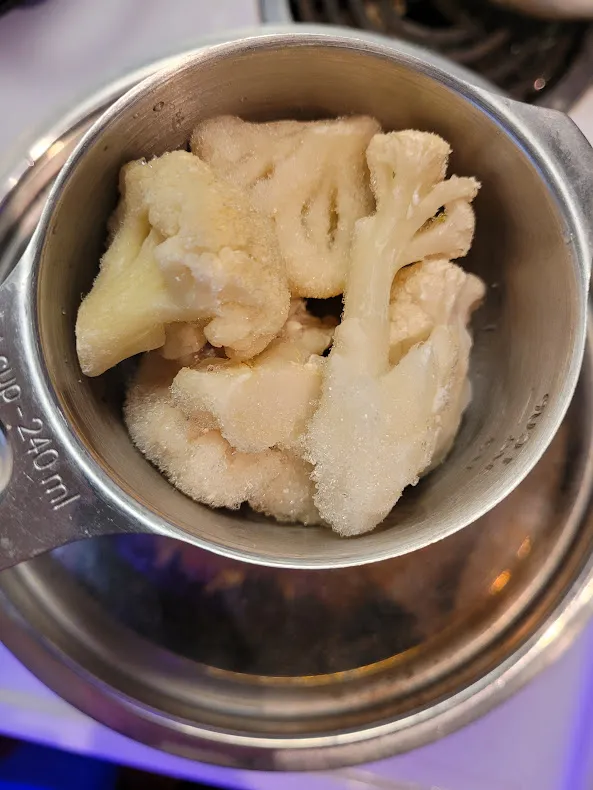 Frozen Caulitflower defrosting in a measuring cup on lid of pot of boiling water