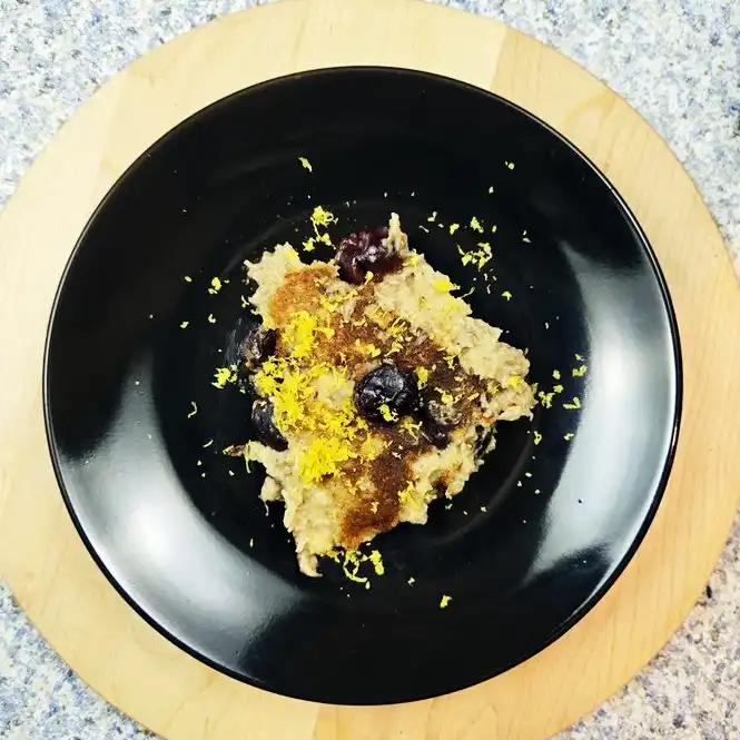 Plant Based Dark Cherry Clafoutis on a black plate dusted with cinnamon and lemon zest